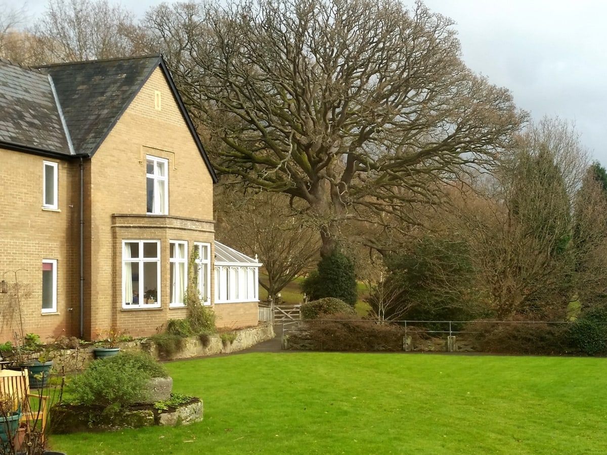 The stone house with its bay window and conservatory, seen across the lawn