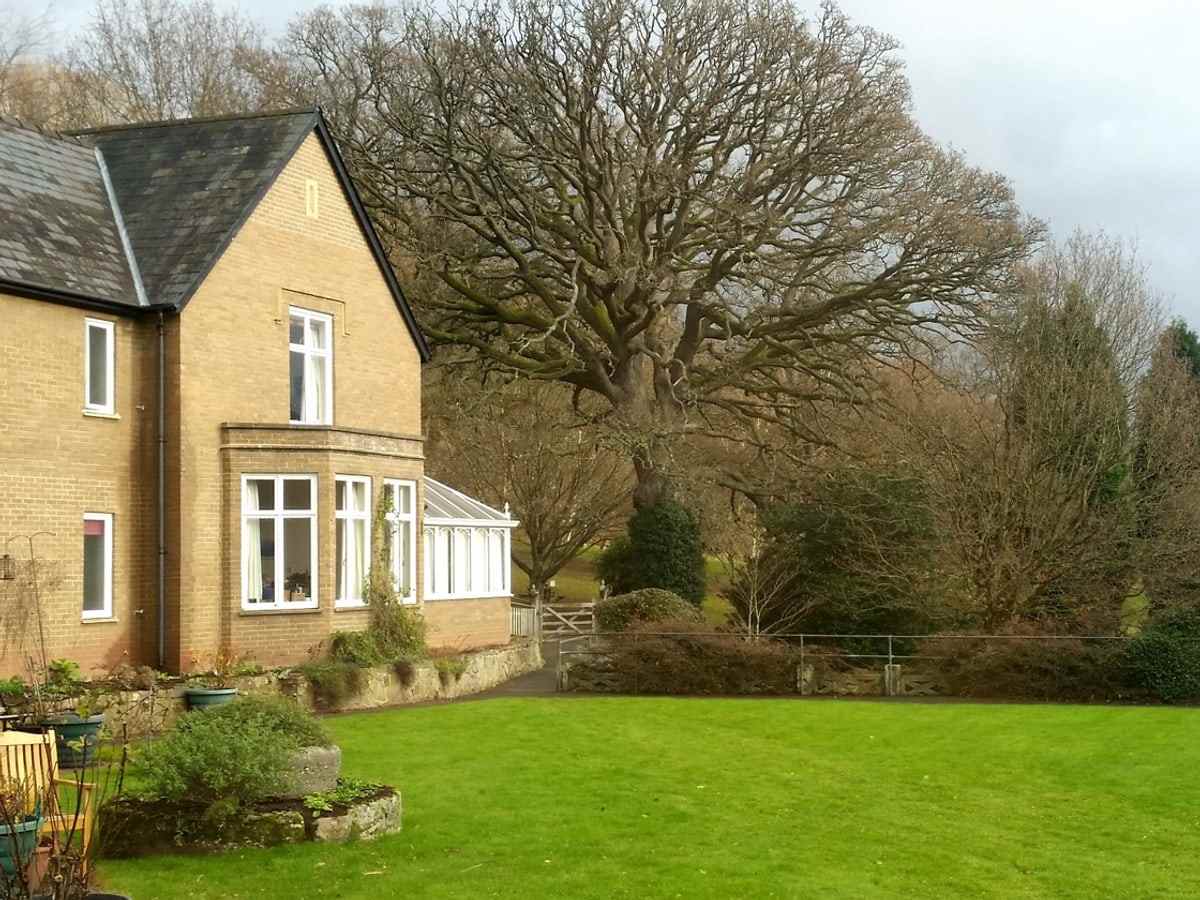 The stone house with its bay window and conservatory, seen across the lawn