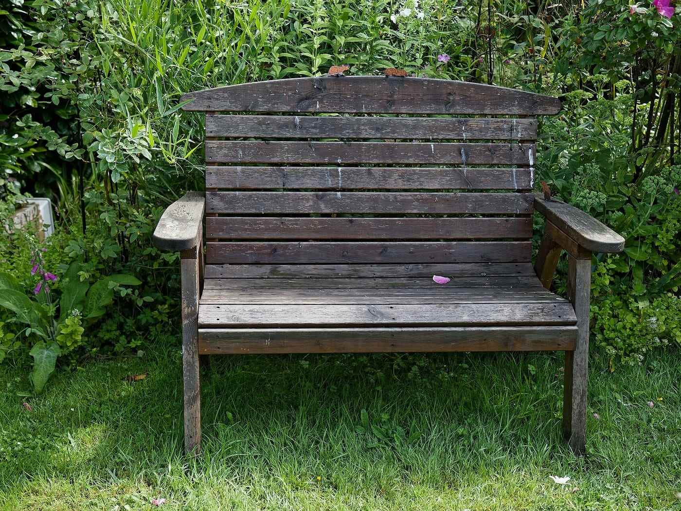 A weathered wooden garden seat set back into a deep planted border