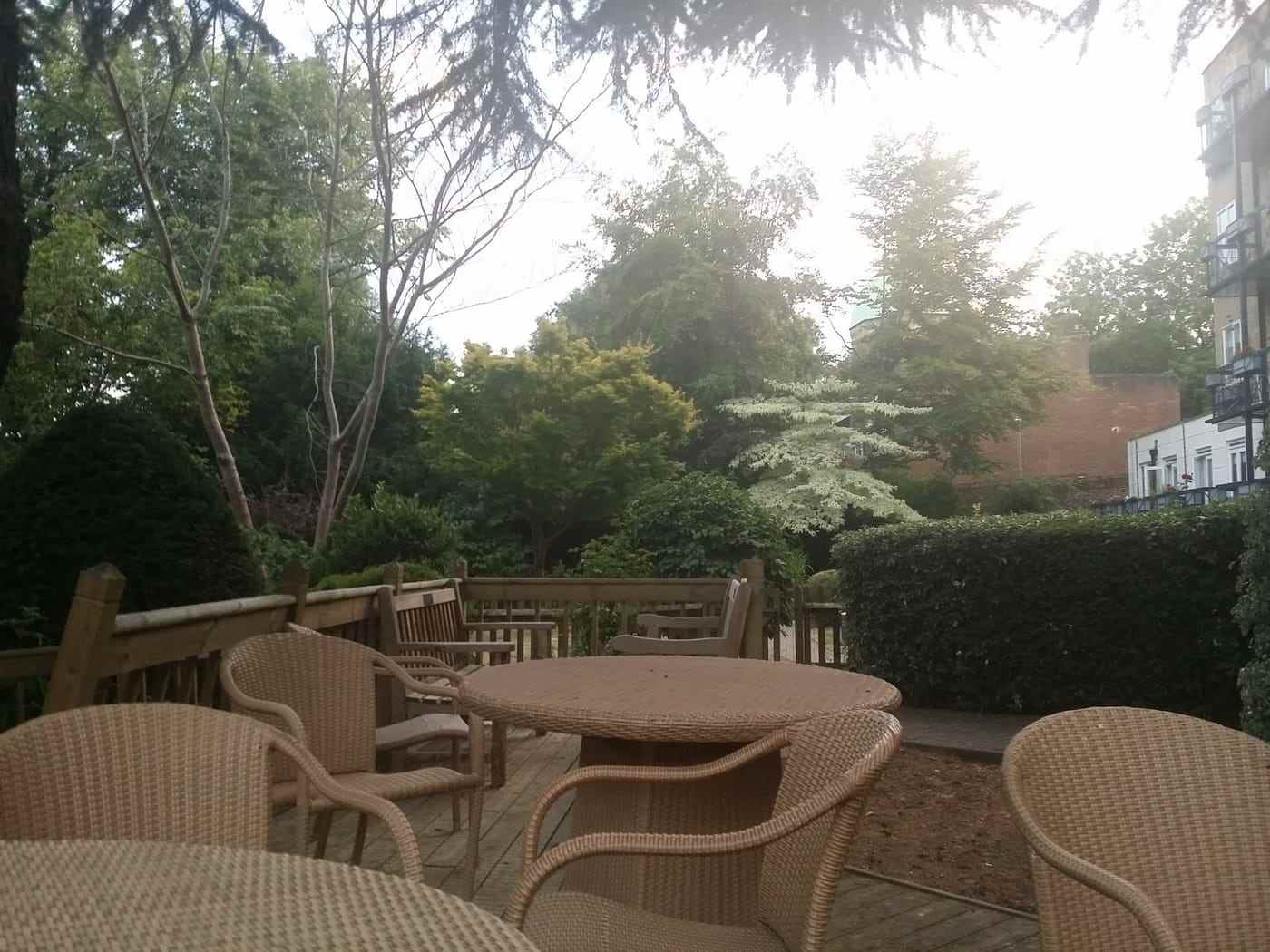 Wicker chairs and a table on the terrace, facing a lawn edged with clipped hedging