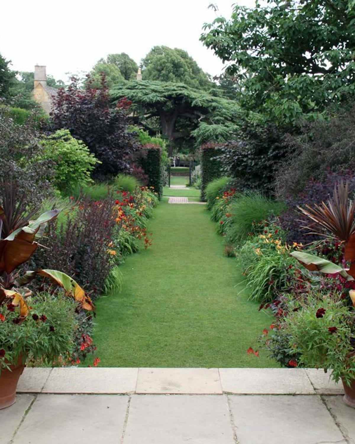 A mown grass path running between deep borders towards a gate
